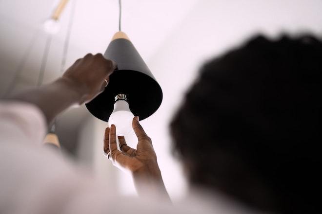 Person schraubt eine LED-Lampe in einen Lanpenschirm.