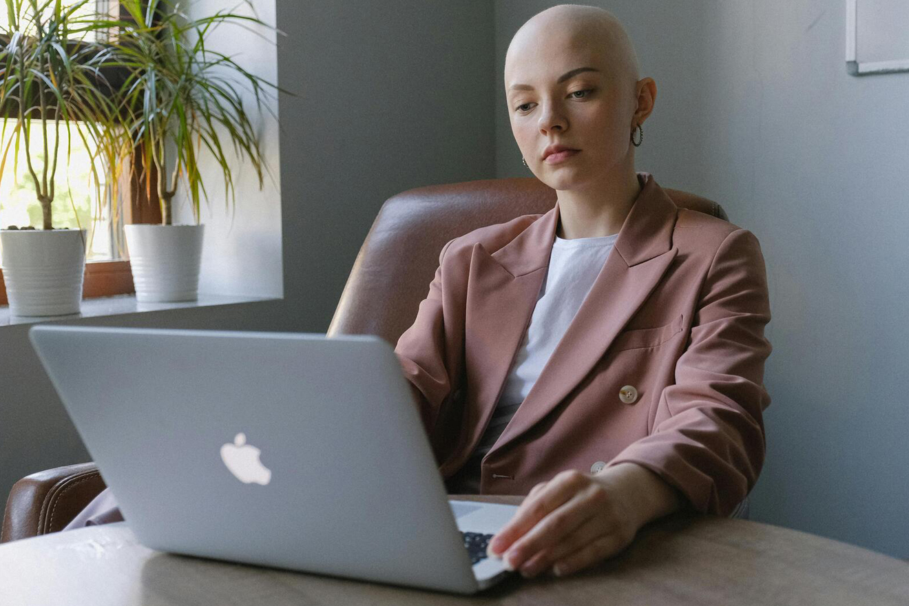 Frau mit Glatze sitzt vor ihrem Mac-Computer