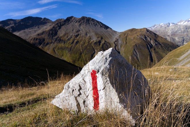 Auf einem Stein mitten in den Bergen ist ein weiss-rot-weisses Kennzeichen aufgemalt