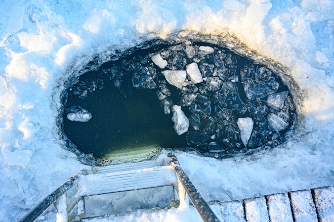Ein Loch in eienr Eisdecke im See, in das eine Leiter hinunterreicht