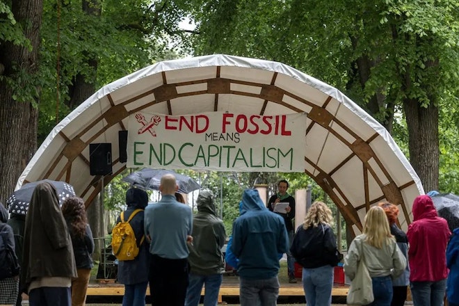 Studierende besetzen den Petersplatz in Basel und stehen unter einem Zelt mit dem Banner «End Fossil Means End Capitalism»