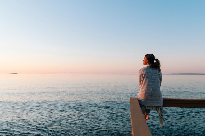 Frau sitzt auf einem Gelände und schaut über den See