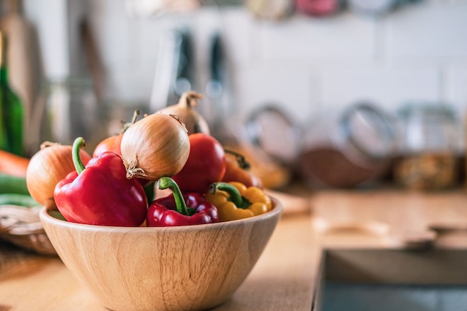 Eine Holzschale mit Peperoni und Zwiebeln steht in einer Küche