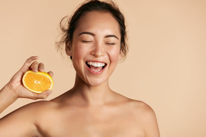 Lachende Frau mit halber Orange in der Hand