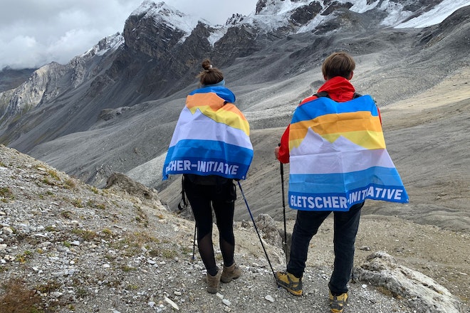 Zwei Personen mit Initiativ-Fahne der Gletscher-Initiative in den Bergen