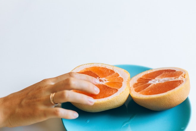 Eine aufgeschnittene Grapefruit auf einem Teller, eine Hand legt den Finger in die Frucht.