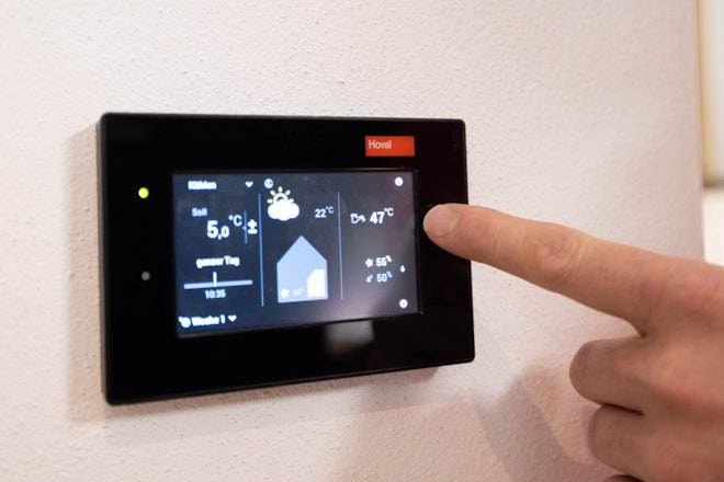 Ein Touchscreen mit Temperaturanzeigen fürs Haus und eine Hand, die darauf tippt