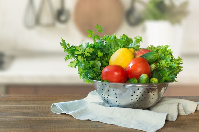 Ein Sieb mit Salat, Tomaten, Gurken und einer Zitrone in der Küche