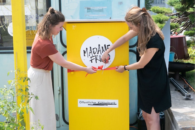 Zwei Frauen schneiden eine Schleife um einen öffentlichen Kühlschrank durch