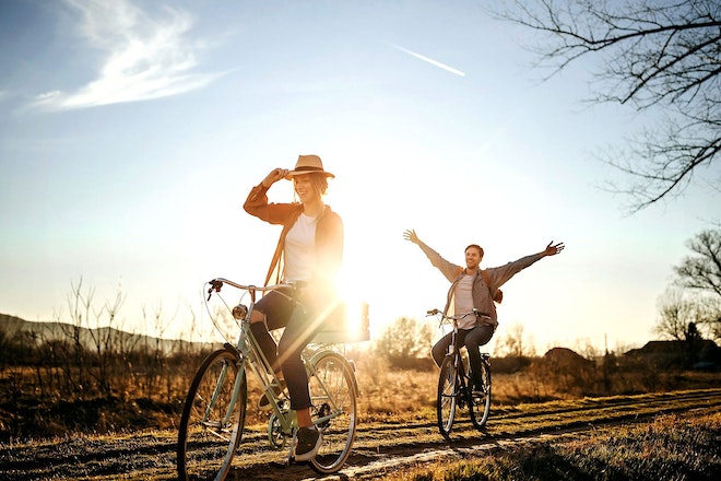 Zwei Personen fahren Fahrrad auf einem Feldweg bei Sonnenaufgang