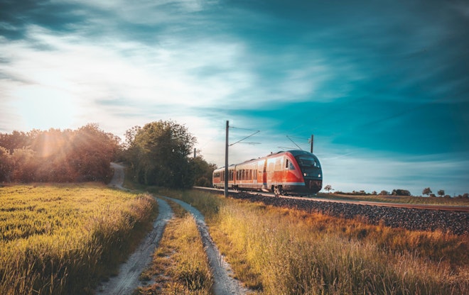 Ein Zug zieht an einer Landschaft mit einem Naturweg drin vorbei