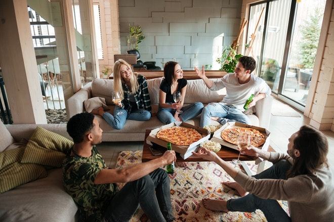 Junge Menschen sitzen im Wohnzimmer zusammen und essen Pizza