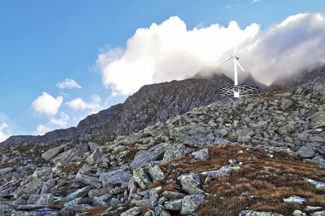 Ein Windkraftwerk mit Photovoltaikmodulen rund um seinen Sockel steht mitten im Geröllfeld eines Berges 