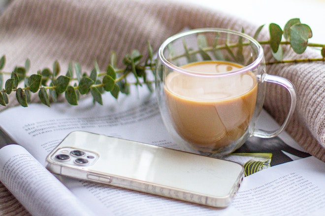 Eine Tasse Milchkaffe und ein cremefarbenes I Phone liegen auf einem Magazin