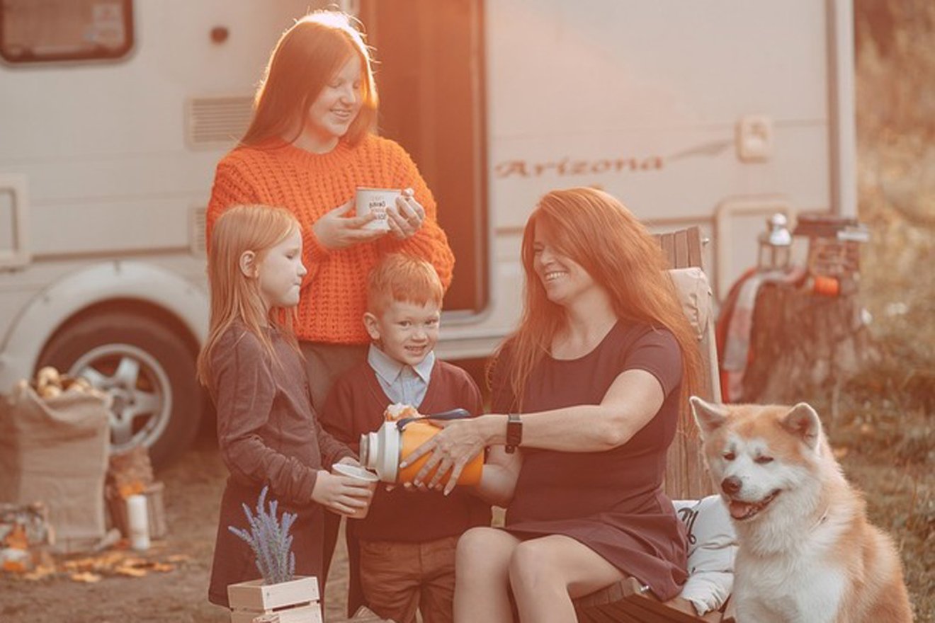 eine Familie mit Hund trinkt Tee vor dem Camper