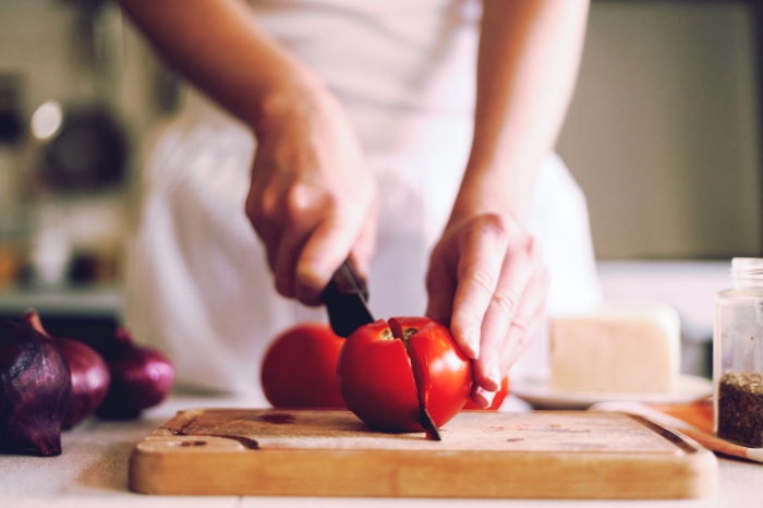 Eine Frau schneidet in der Küche eine Tomate in zwei Hälften