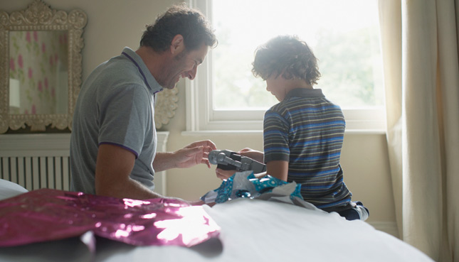 Vater und Sohn sitzen auf dem Bett und packen einen Spielzeugroboter aus