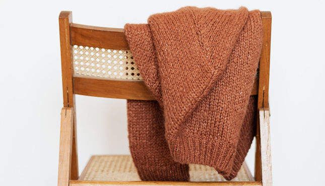 Ein rostfarbener Wollpullover über einer Stuhllehne