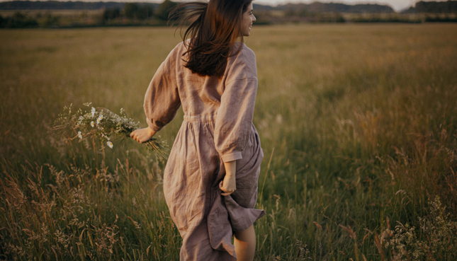 Frau im Leinenkleid läuft über eine Sommerwiese