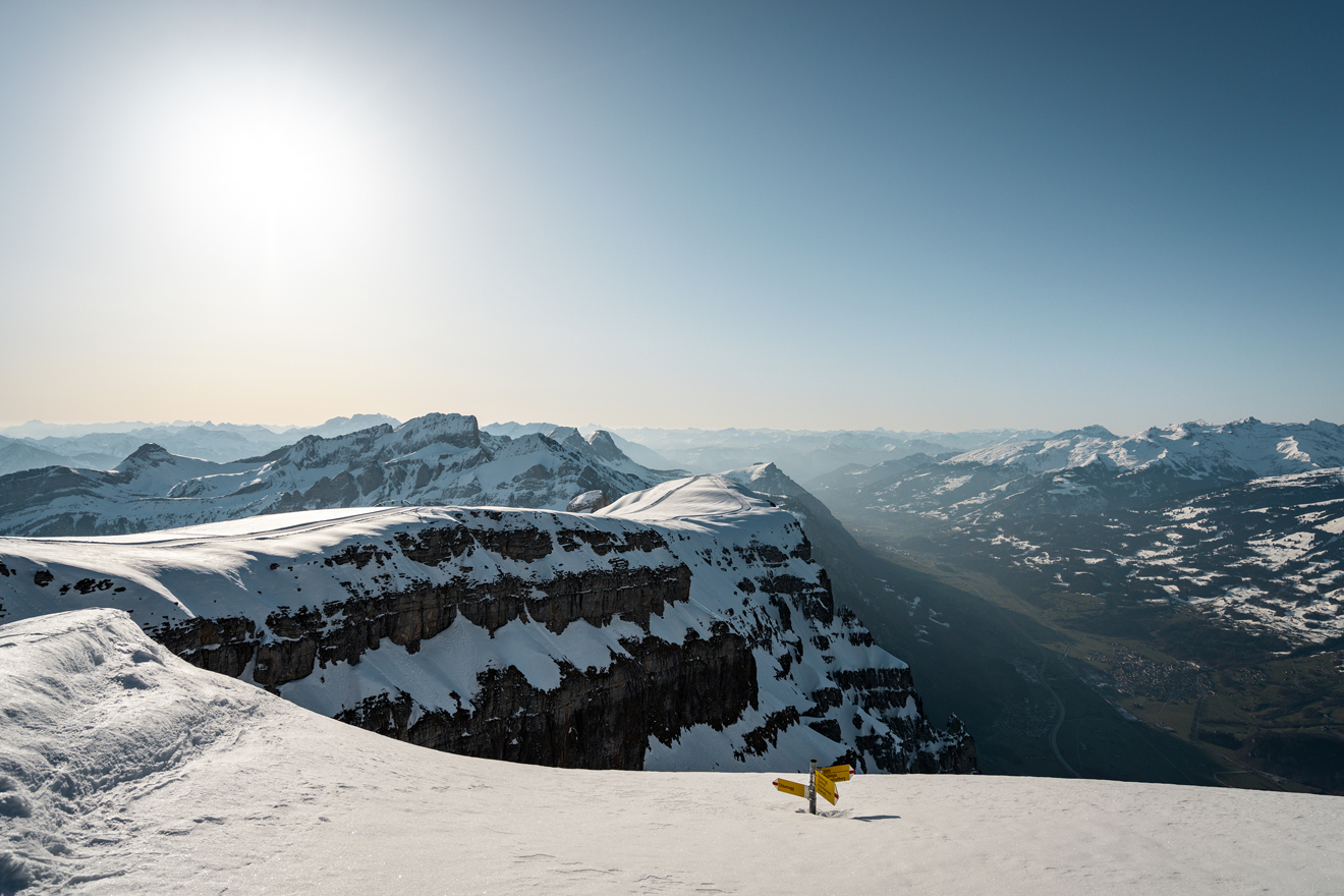 Bergpanorama mit Blick ins Tal – ein Wanderwegweiser ist bis fast oben hin zugeschneit