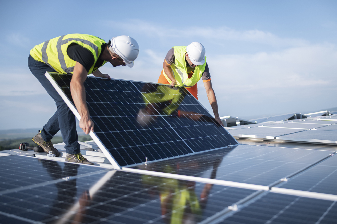 zwei Männer installieren ein Solarpanel auf einem Dach