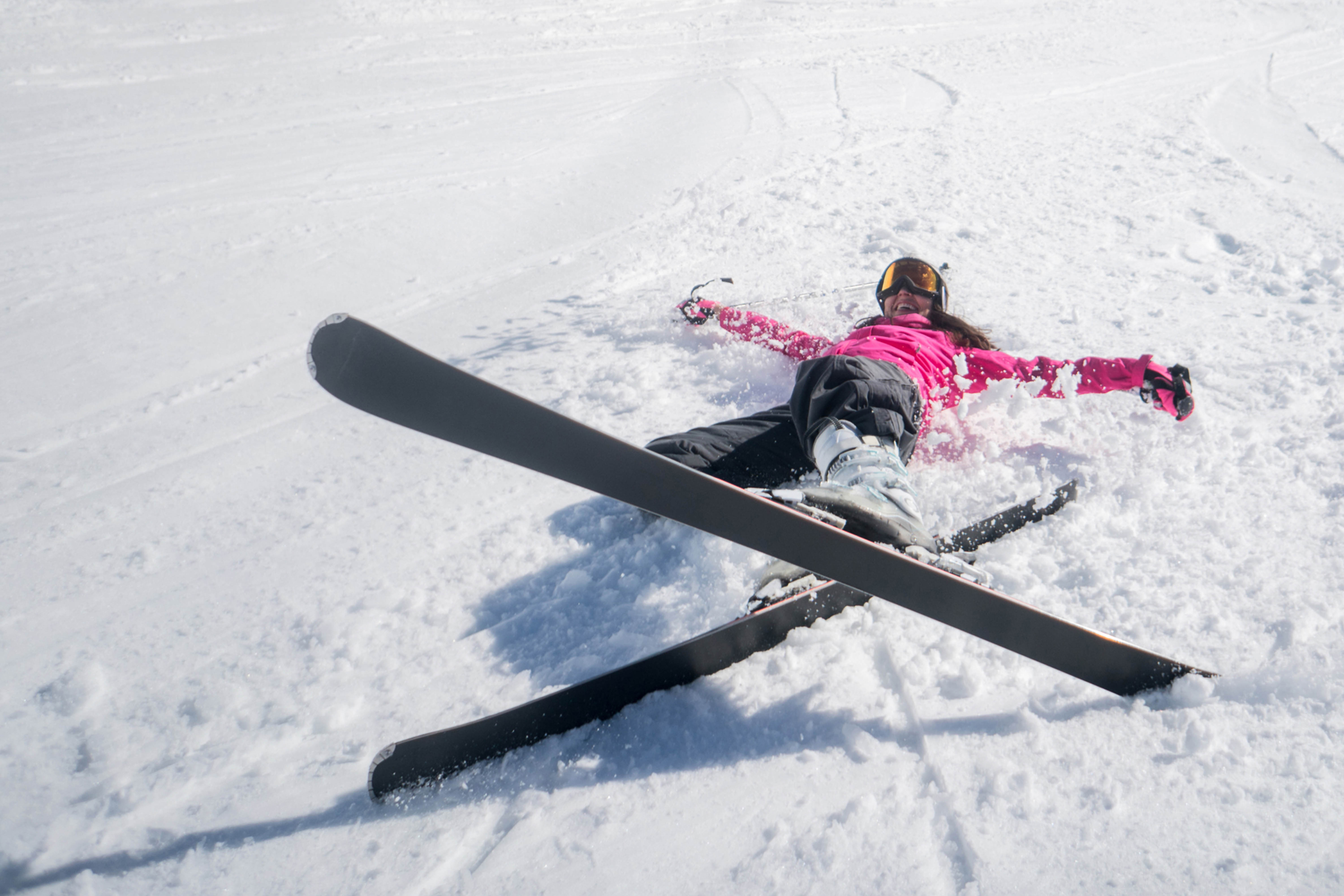 eine lachende Skifahrerin liegt au der Piste und kreuzt die Skier