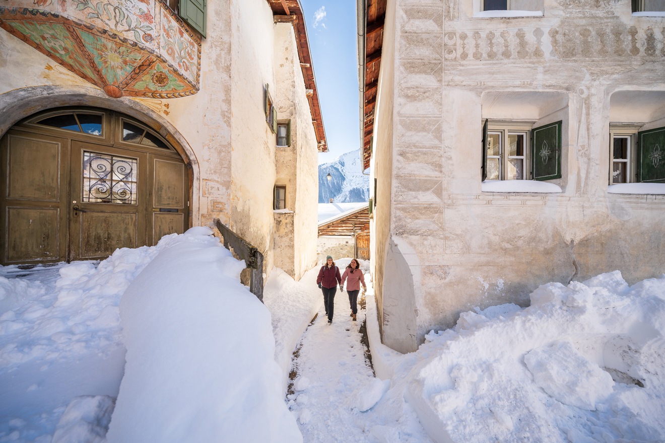 zwei junge Frauen stapfen in einem Engadiner Dorf durch den Schnee