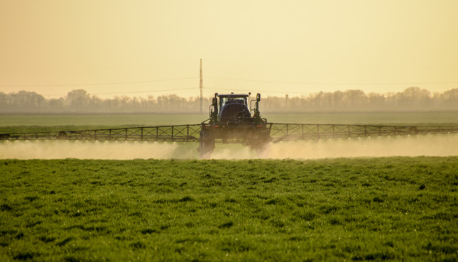 Traktor versprüht Pestizide auf einem Feld.