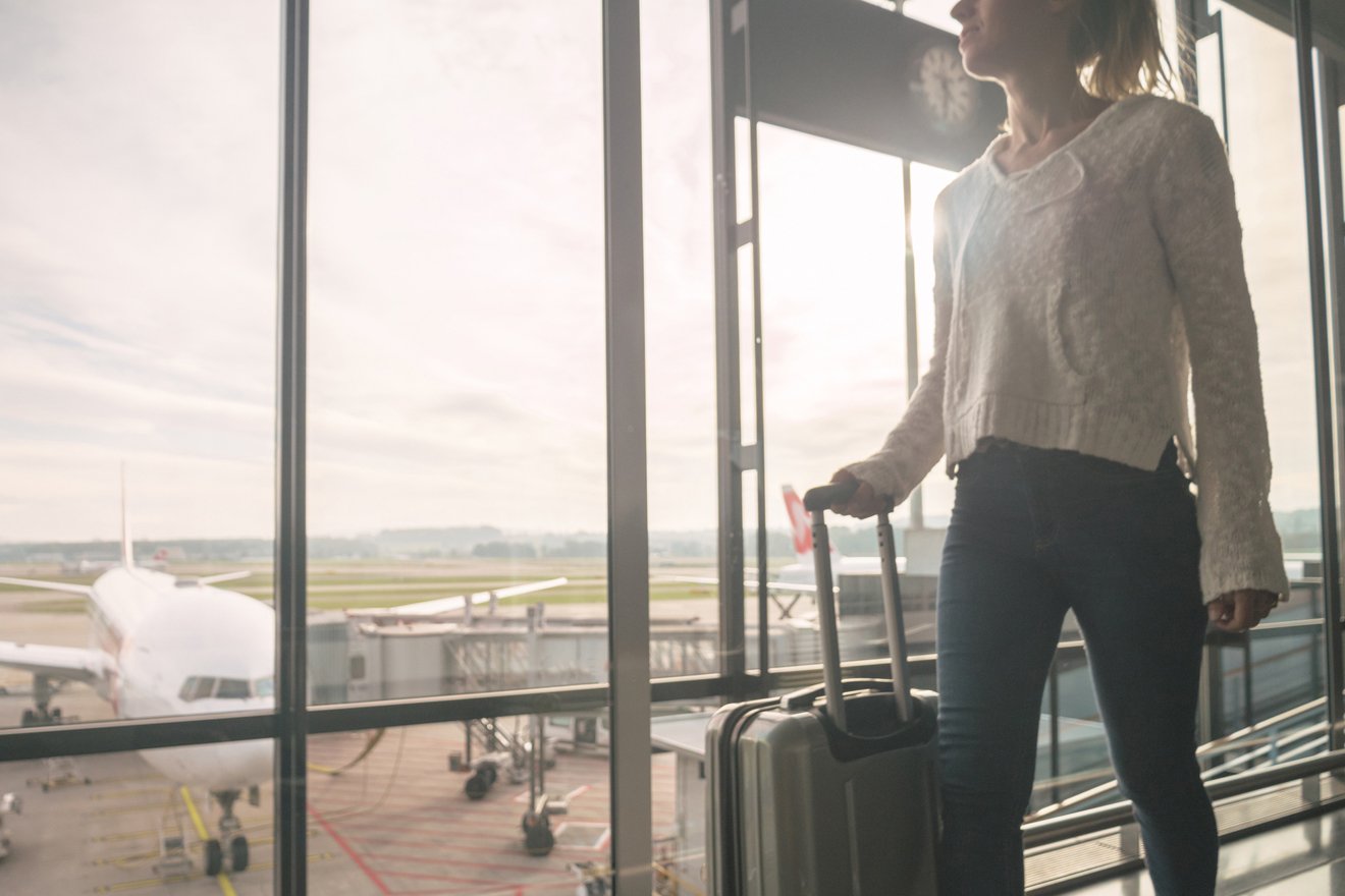 eine Frau steuert mit einem Rollkoffer in der Hand ein Flughafengate an