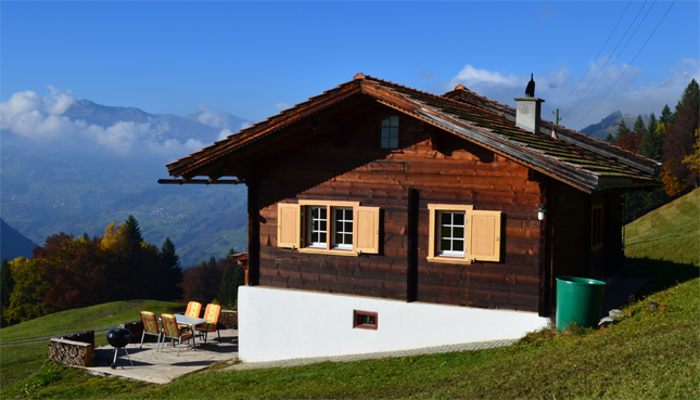 Eine Hütte steht an einem Hügelkamm - im Hintergrund ein wunderschönes Bergpanorama