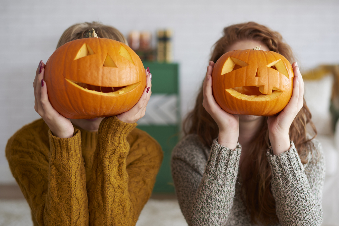 zwei Frauen verstecken ihre Gesichter hinter Halloween-Kürbissen