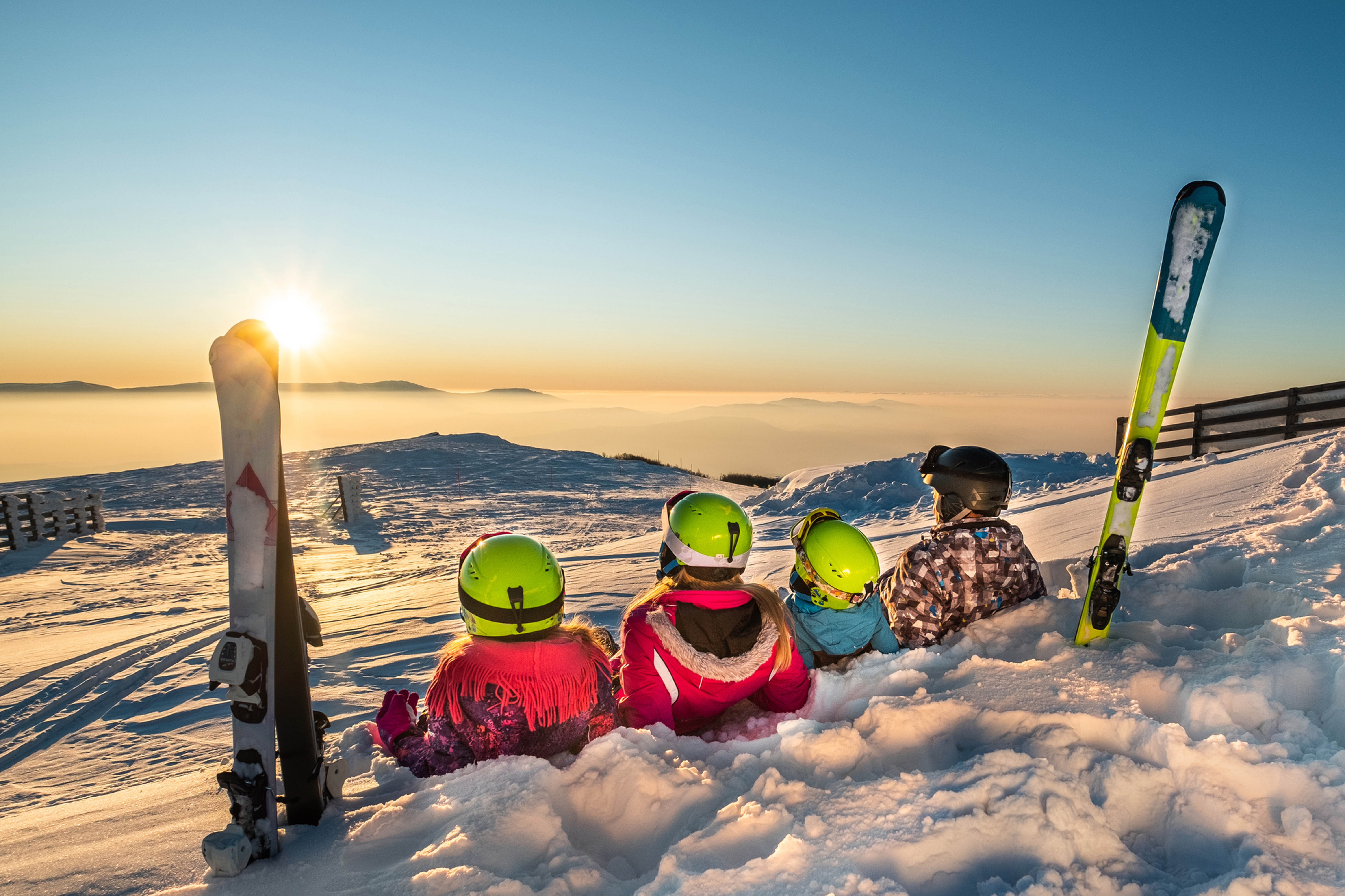 Eine Familie sitzt in Skikleidung im Schnee und schaut in die Ferne.